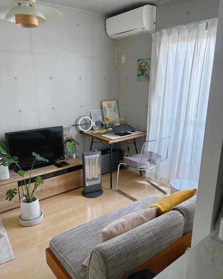 木目調の床とグレーのソファが配置されたモダンでナチュラルなリビング、透明なチェアが抜け感を演出する印象的な空間