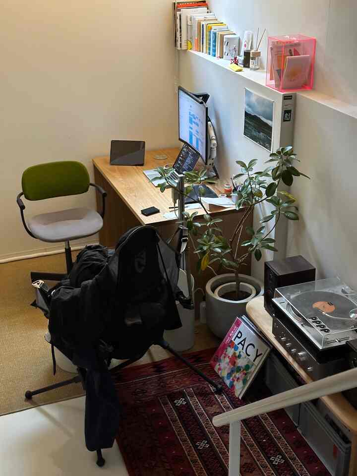 白い壁と木製の机が配置されたコンパクトなホームオフィスワークスペース、緑の椅子と観葉植物が自然な雰囲気を演出する空間