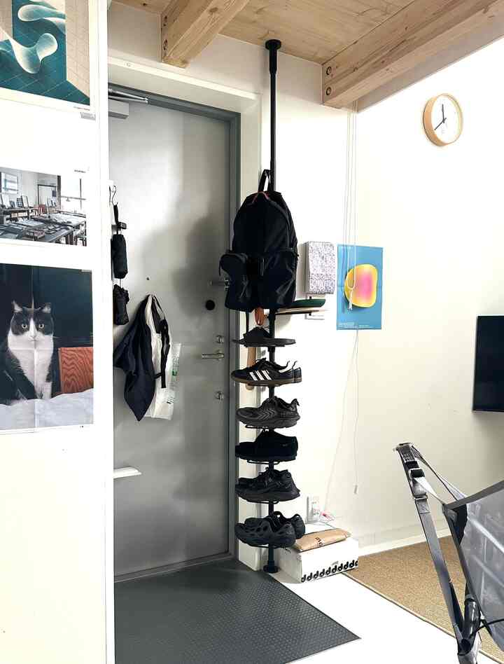 明るい白い壁と黒の縦型シューズラックが配置されたコンパクトで整理された玄関スペース