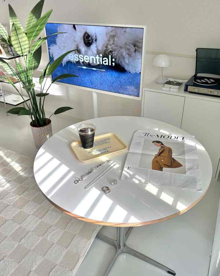 白とナチュラルカラーのモダンな丸形ダイニング、丸い食卓とテレビ台、観葉植物が配置された明るい空間