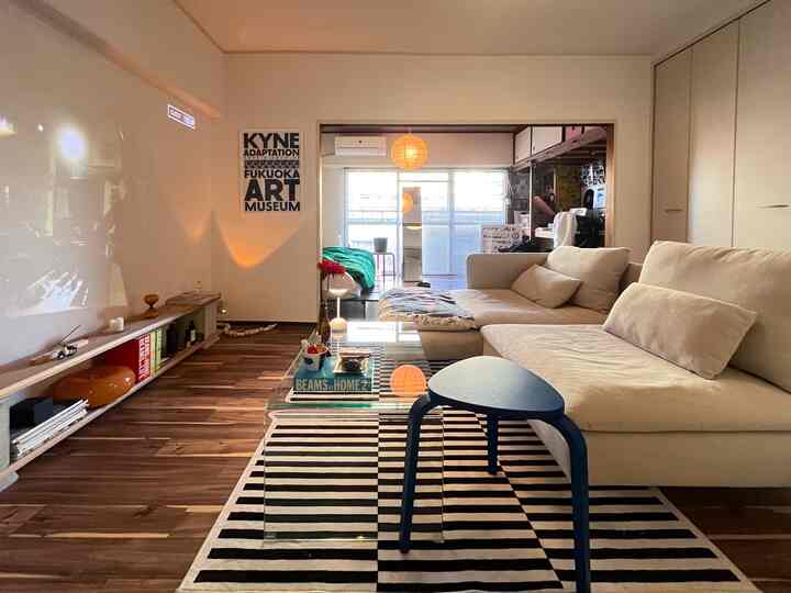 ベージュのソファとダークブラウンの木床、ストライプのラグがあるモダンで居心地の良いワンルームリビング