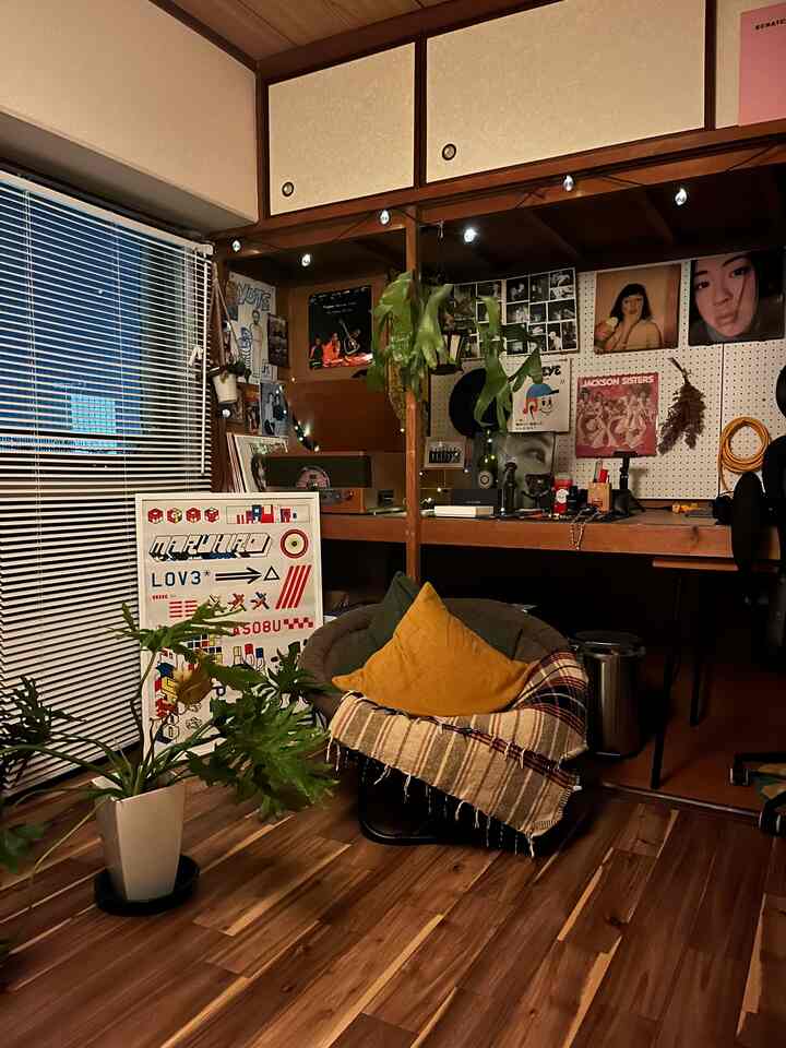 温かみのある木目調と多彩なポスターが調和するアットホームなワンルーム、植物とストリングライトが映える収納アイデアのある空間
