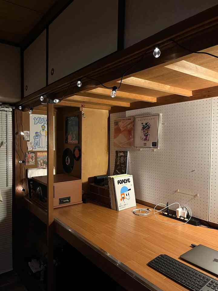 ナチュラルカラーのコンパクトなホームオフィス、木製デスクと有孔ボードの壁にポスターとターンテーブルが配置された雰囲気のある空間