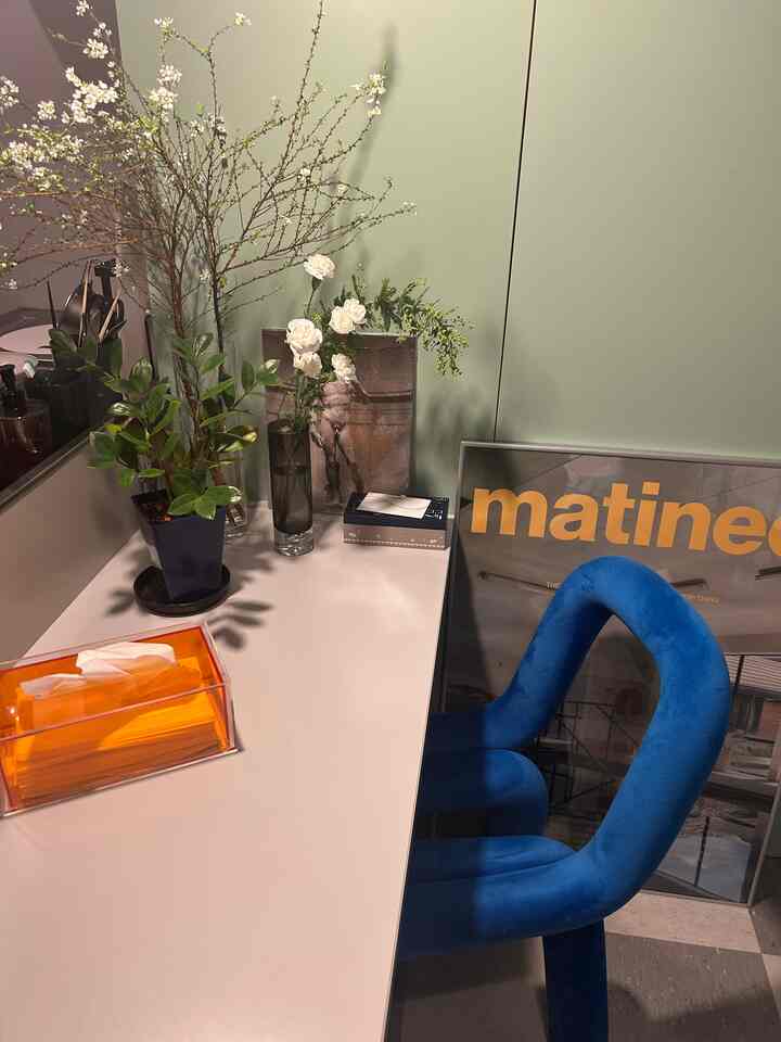 ベージュ色の壁と白いカウンターがある一人暮らしのダイニング、青いベルベットのダイニングチェアと花瓶が配置された印象的な空間