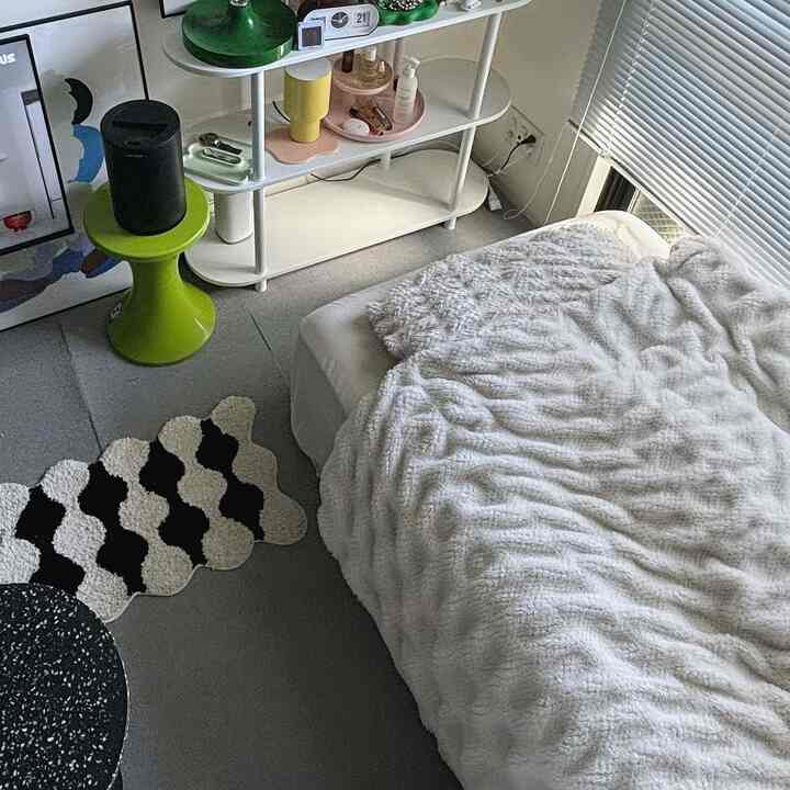 モノトーンの寝室、白い掛け布団カバーのベッドと白い棚、窓際のブラインドが配置された雰囲気のあるインテリア