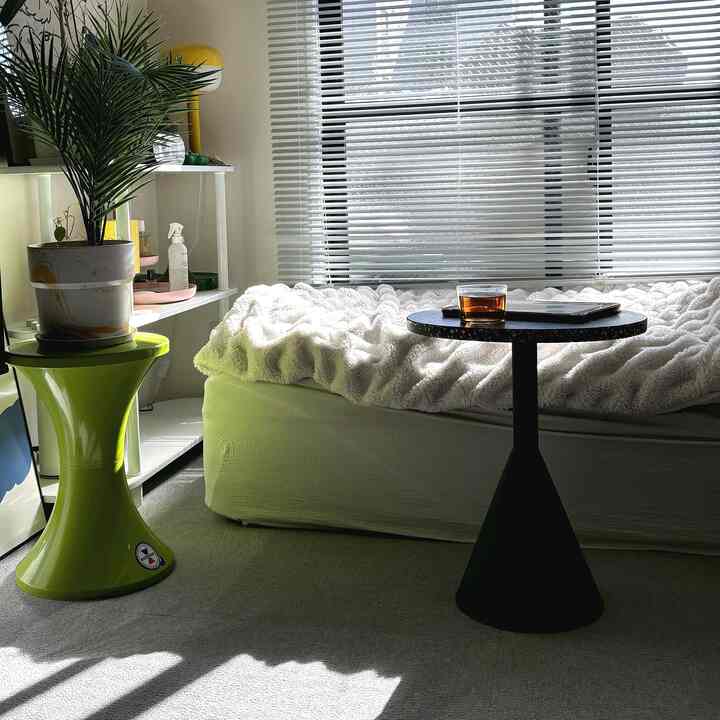 白と緑のトーンのリビング、ブラインドの窓とサイドテーブル、植物が配置された自然で落ち着いた空間