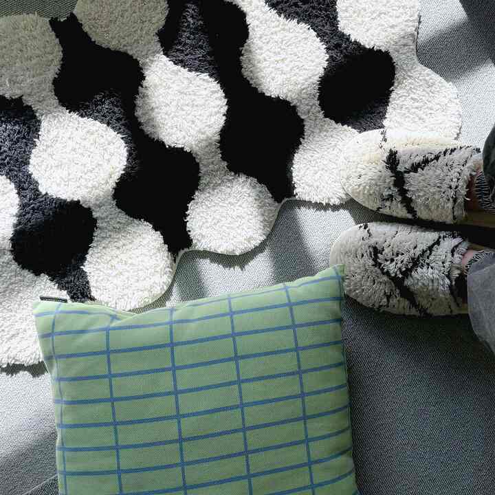 グレーの床にモノトーンの白黒ラグと緑のチェック柄クッションが配置され、スリッパが置かれた落ち着いた空間