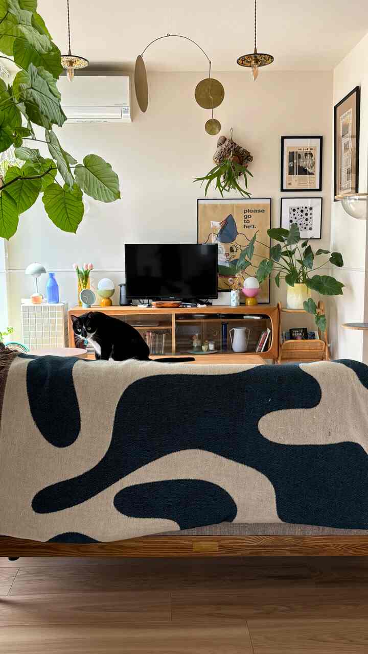 白い壁と木目調家具が調和するミッドセンチュリーモダンのリビング、ソファの背もたれに猫がいる雰囲気のあるインテリア