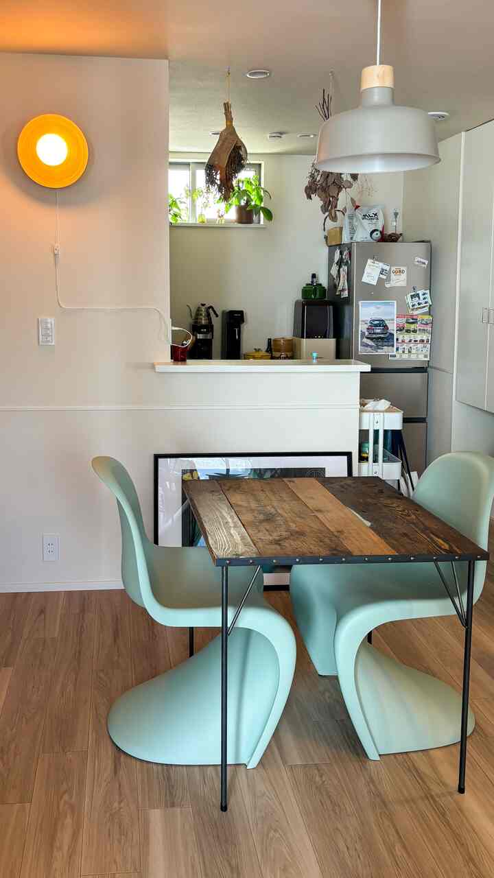 木目調の床とスカイブルーのパントンチェアが配置されたダイニングルーム、黄色い壁照明がアクセントの雰囲気ある空間