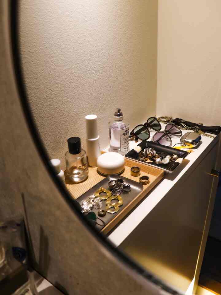 温かみのあるアイボリーの壁と木製トレイに香水や指輪、サングラスなどの小物が整理されたパウダールームスペース