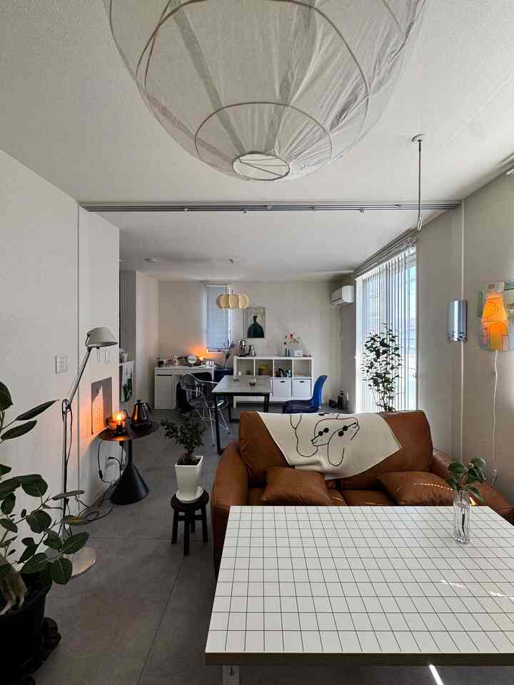 ナチュラルな色調の12畳のリビングダイニングルーム、ブラウンのソファとホワイトの格子柄コーヒーテーブル、植物とペンダントライトが配置されたモダンで落ち着いたインテリア