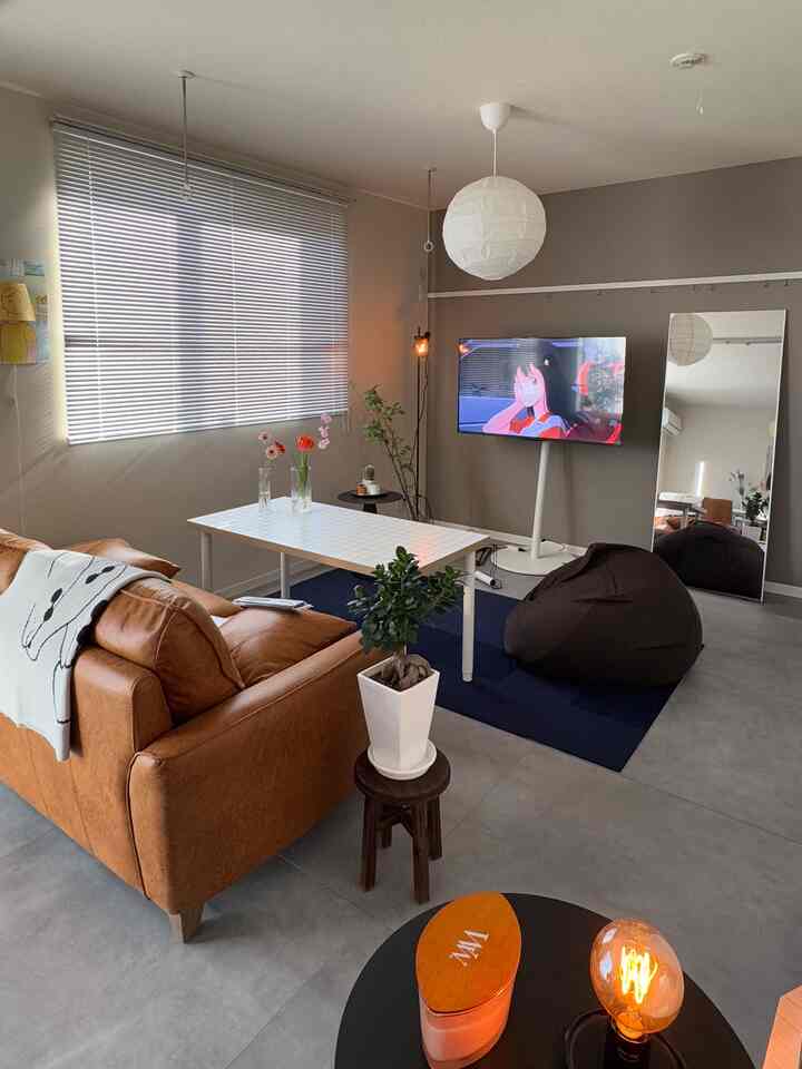 グレーの壁と床、ブラウンのソファとビーンバッグがネイビーのラグ上に配置されたモダンなリビングルーム。