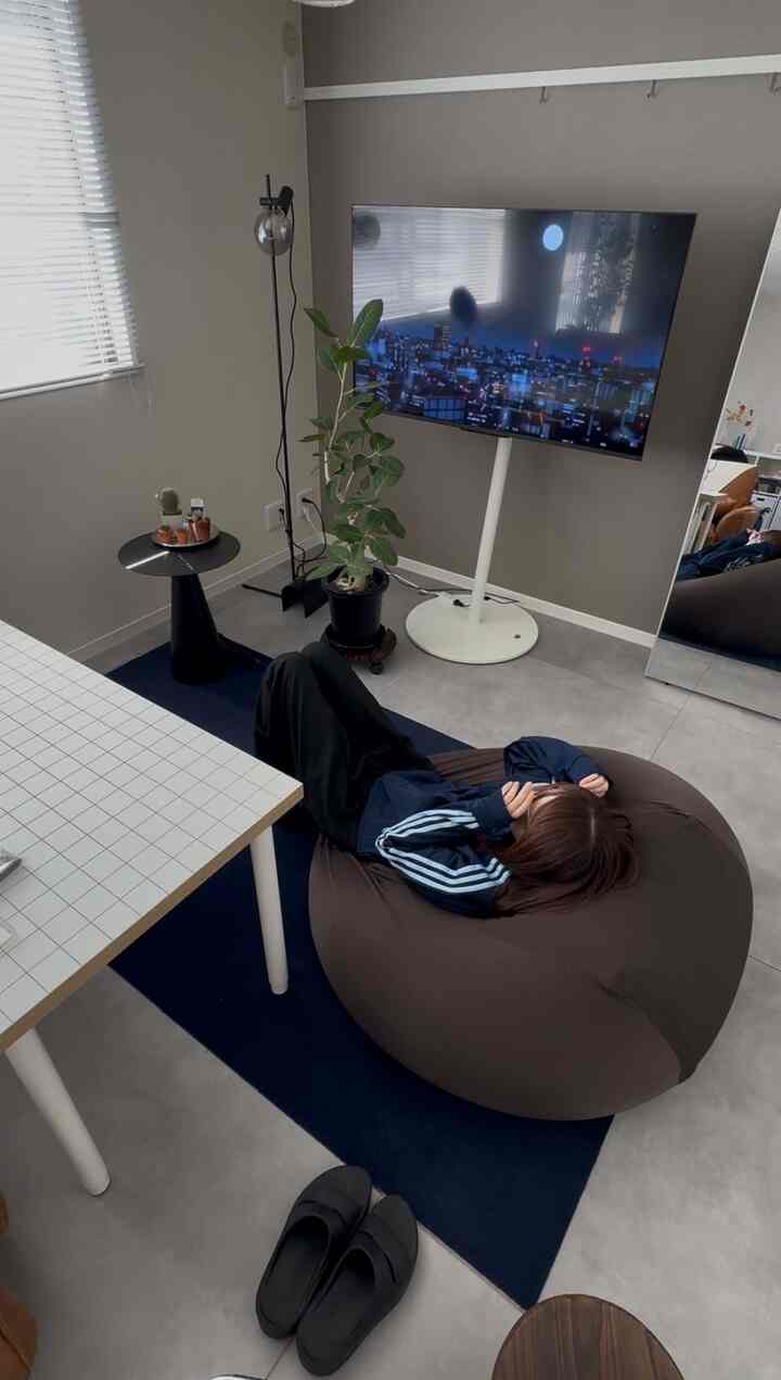 グレーとブルーのトーンのワンルームリビング、大型テレビとブラウンのビーズクッション、サイドテーブルが配置された落ち着いたモダンな空間