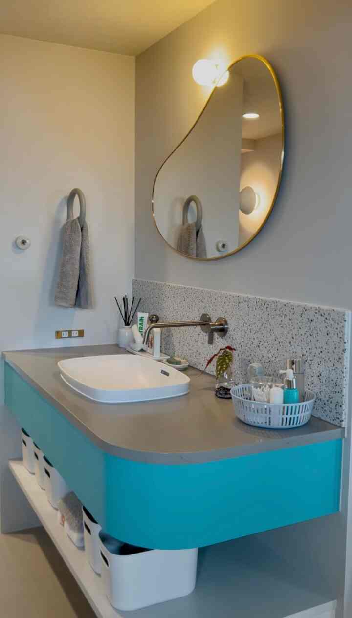 白い壁とミント色の曲線洗面台があるバスルーム、丸みを帯びた不規則な鏡と壁灯が調和する清潔感のあるインテリア