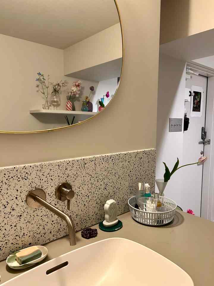 白とグレー調のバスルーム、ゴールド枠の鏡とテラゾーバックグラウンド、上品な水栓とナチュラルな装飾が調和した空間