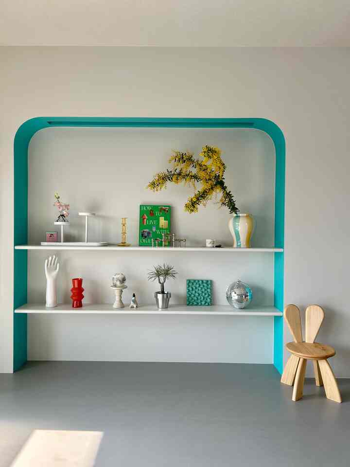 白とミント色調の寝室兼ワークスペース、アーチ型ニッチ棚に飾られたオブジェがあるミニマルなインテリア