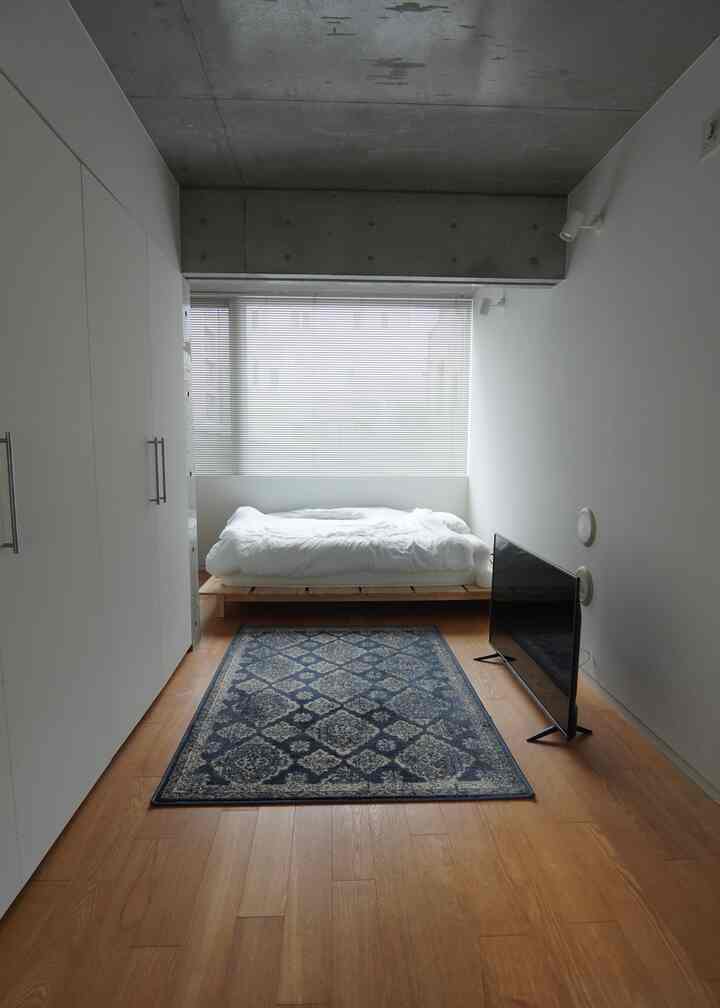 白とウッドトーンが調和したシンプルな6畳の寝室、低いベッドとブラインドが配置されたモダンなインテリア