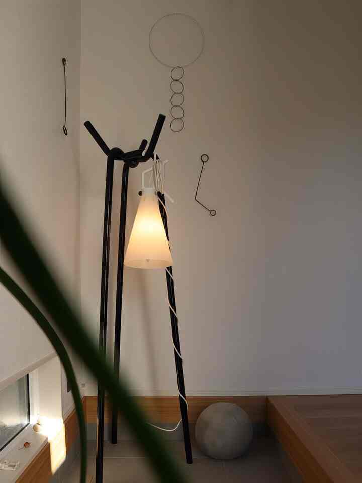 ナチュラルカラーの壁と木目調の下部仕上げがある玄関に、黒いコートハンガーと明るい間接照明のランプが配置された雰囲気のある空間