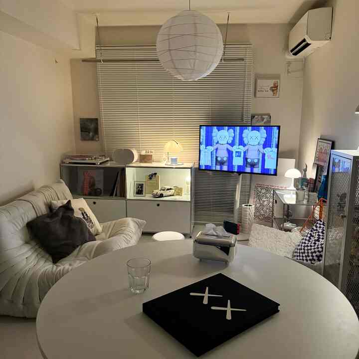 白を基調としたコンパクトなリビングルーム、ホワイトソファと円形コーヒーテーブル、壁掛けテレビとモダンな収納が配置された空間