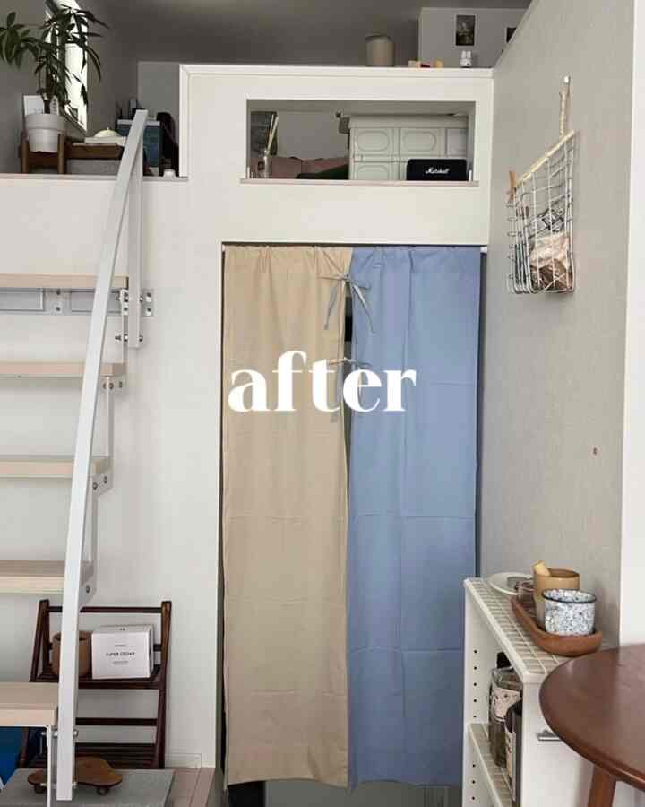 ベージュとブルーのカーテンで仕切られたナチュラルな色調のロフト空間、階段と居心地の良いキッチンコーナーがあるインテリア