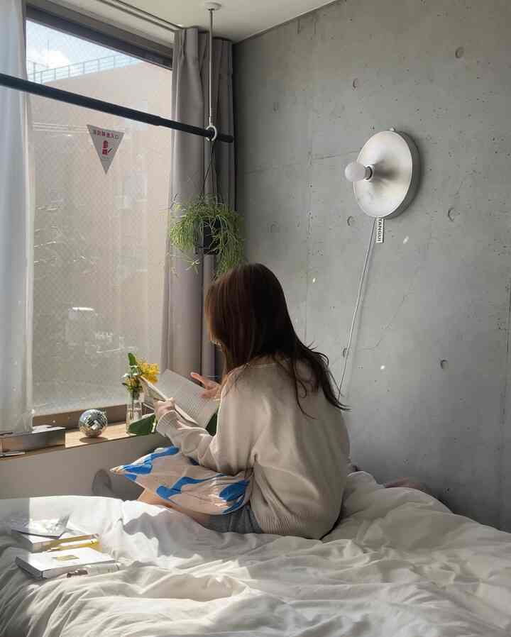 温かみのある光を放つシルバーの壁照明がある寝室、白い寝具と本を読んでいる人がいる落ち着いた空間