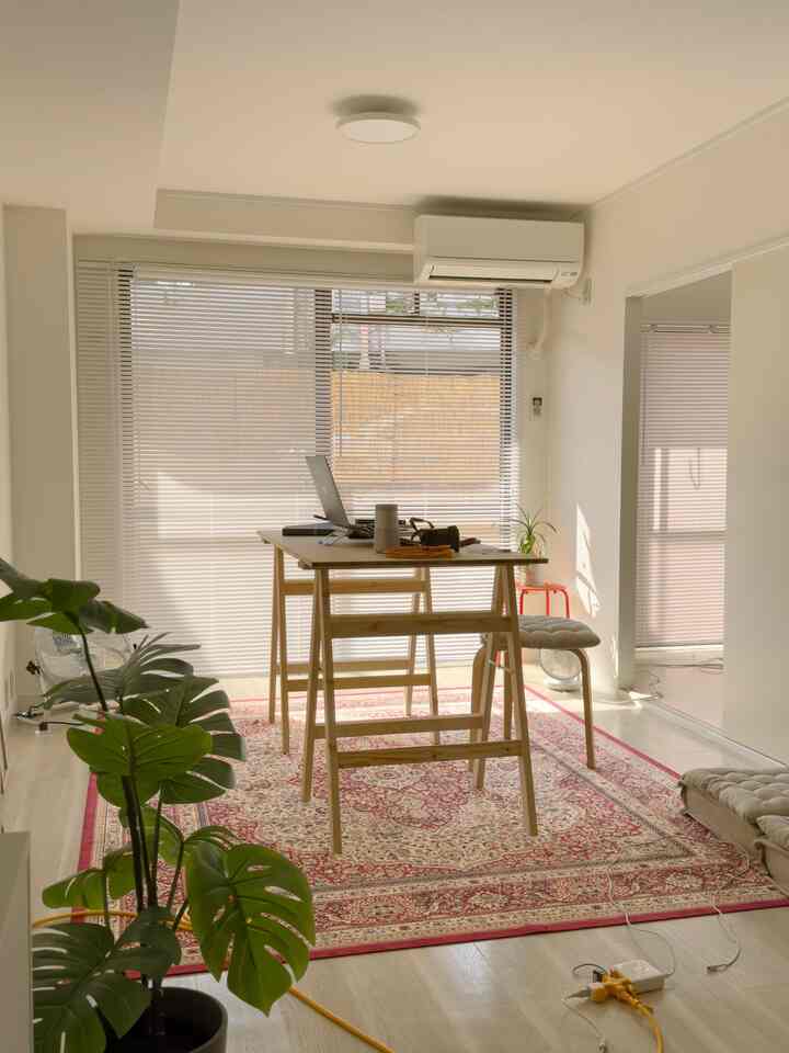 ベージュと赤のトーンが調和したホームオフィス、モンステラの植物と木製の机が配置された温かみのある作業空間