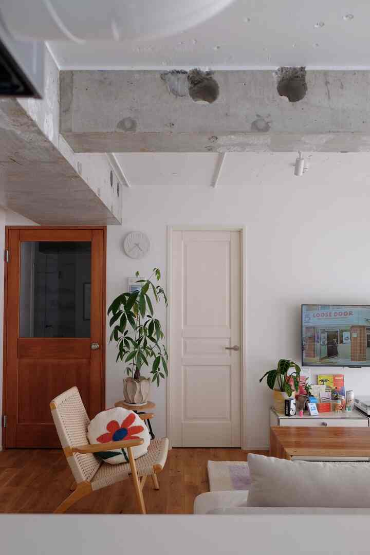 白い壁と木目調の床が特徴のリビング、編み込みのアームチェアと植物が配置されたナチュラルで落ち着いた雰囲気のインテリア