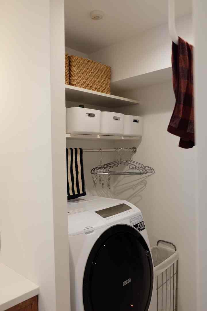白を基調とした狭いバスルーム、洗濯機とシルバー・白の収納ボックス、シルバーのハンガーが整然と配置された雰囲気のあるインテリア
