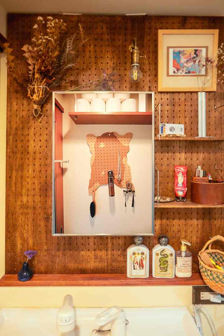 暖かいナチュラルカラーのパウダールーム、木製のペグボード壁に収納棚、壁照明、中央に鏡が配置された雰囲気のあるインテリア