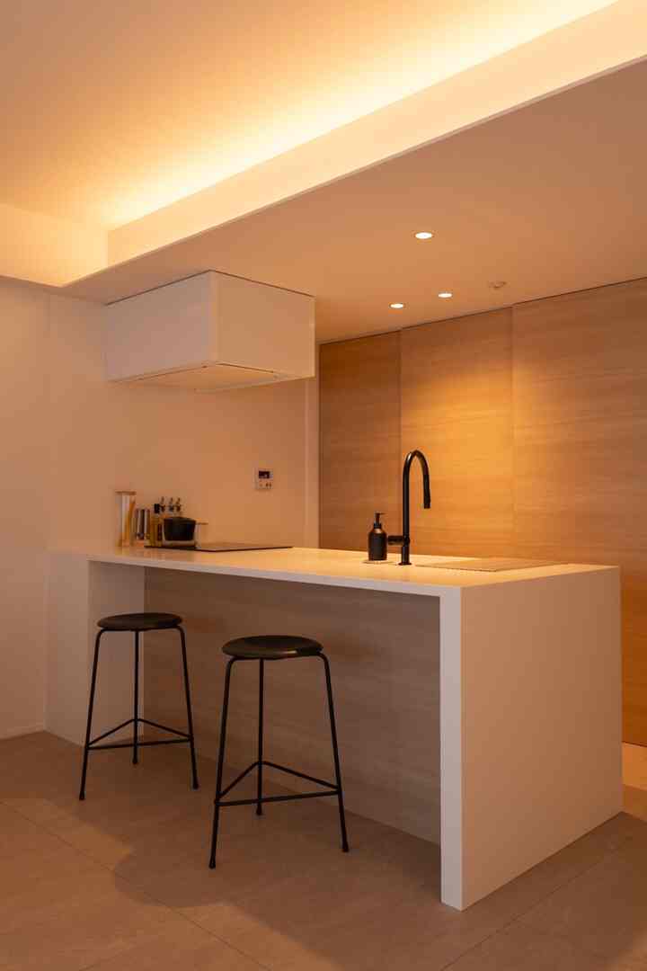 ホワイトとブラウンの色調のキッチン、カフェ風カウンターキッチンと黒いスツールが配された印象的な空間