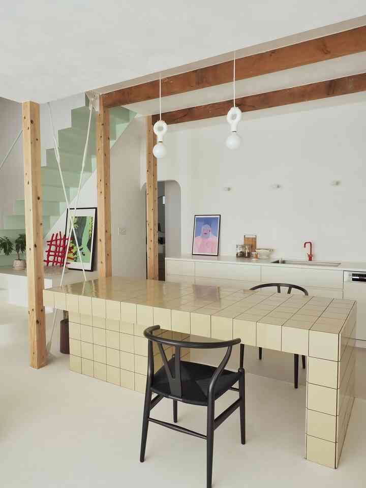 明るいホワイトトーンのキッチン空間に、木製の柱と見える梁があり、タイルのテーブルと黒い椅子が配置された雰囲気のあるインテリア
