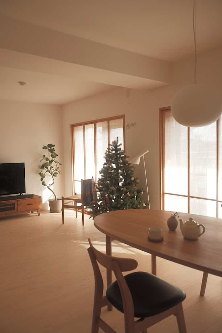 ナチュラルカラーと木目調のシンプルなリビングダイニング、クリスマスツリーと無垢材家具が配置された暖かい雰囲気のインテリア