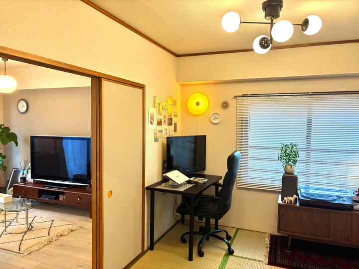明るいホワイトと木目調が調和する6畳の畳の部屋とスライディングドア越しのリビング、リモートワーク用のデスクとオフィスチェアが配置された落ち着いた空間