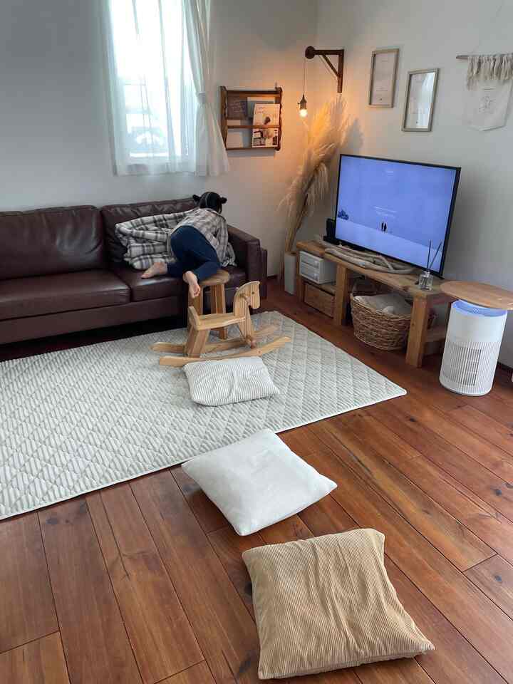 ブラウンのソファと木目調家具、白いラグがあるナチュラルなリビングルームで、ソファに登る子供のいる雰囲気のあるインテリア