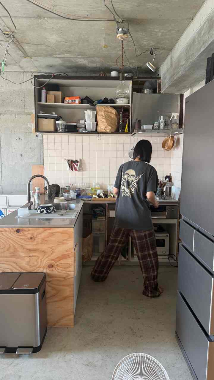 ナチュラルカラーとコンクリートが調和する狭いワンルームキッチン、DIYスタイルの調理スペースで調理する人のいる雰囲気のあるインテリア