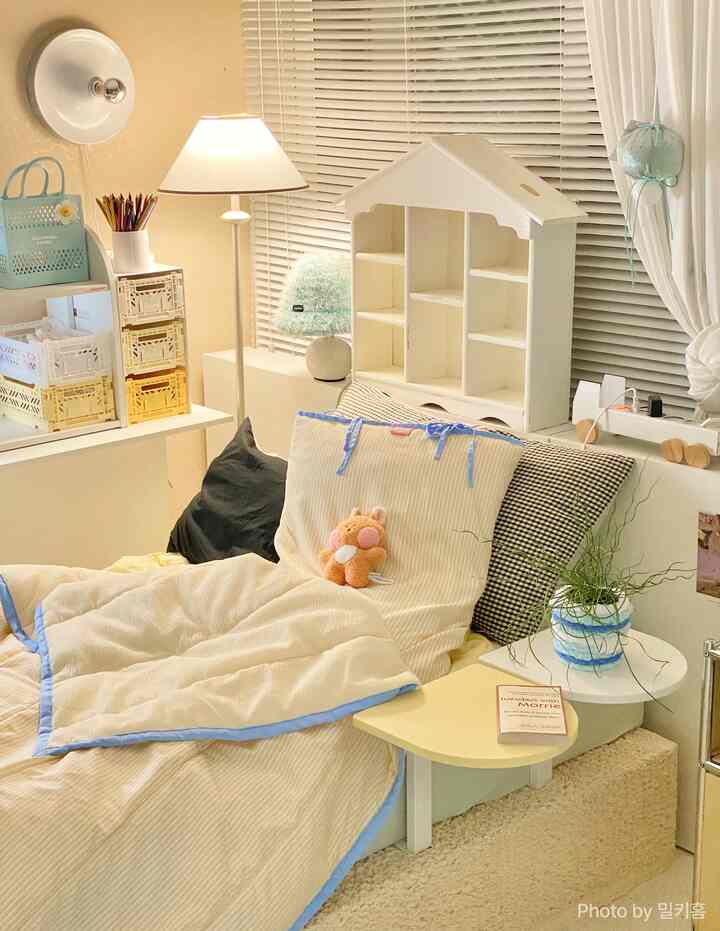 ベージュとホワイトの色調の寝室、枕と寝具が置かれたベッドと子供用人形が配された温かみのある空間