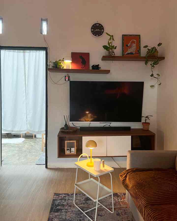 Warm wood tones and white dominate this cozy living room featuring a TV, sofa, side table with lamp, and wall decor with picture frames