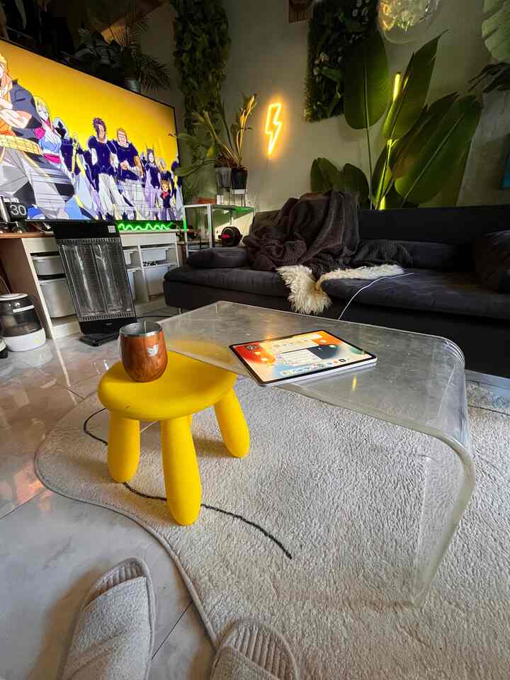 Studio apartment living room with yellow stool, black sofa, plants, and large TV screen creating cozy vibe