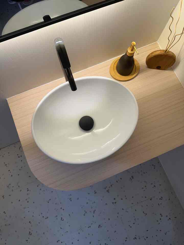 Bright white and natural wood toned bathroom wash basin with a black faucet and decorative objects in a clean space