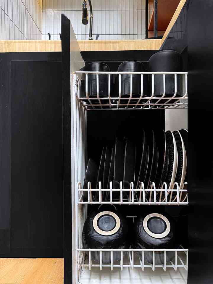 Kitchen interior with black and wood tones, featuring a white metal dish rack neatly organizing various black plates and mugs