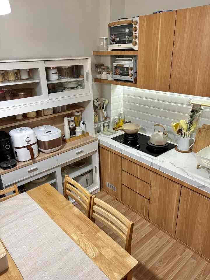 Natural wood-tone and beige kitchen featuring dining table and neatly arranged cooking appliances with a cozy atmosphere