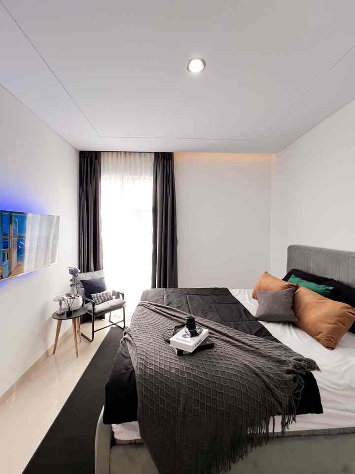 A modern and cozy small bedroom in black and white tones featuring a central bed with side table and armchair nearby