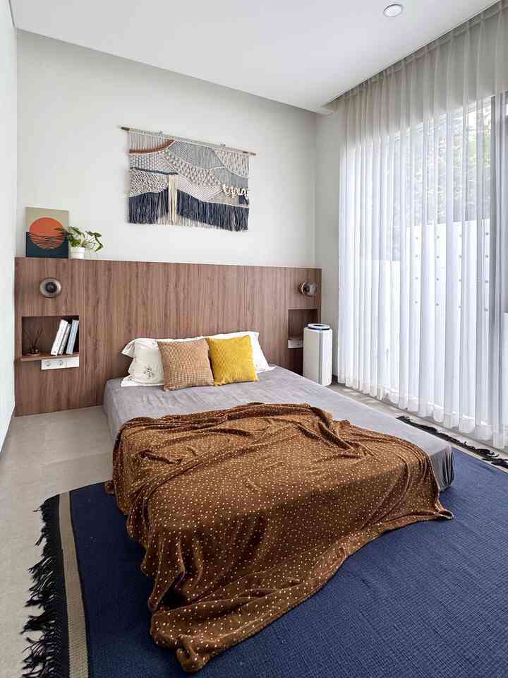 Light gray and brown toned bedroom featuring a floor mattress, cushions on bed, and large macrame wall hanging creating a simple natural atmosphere
