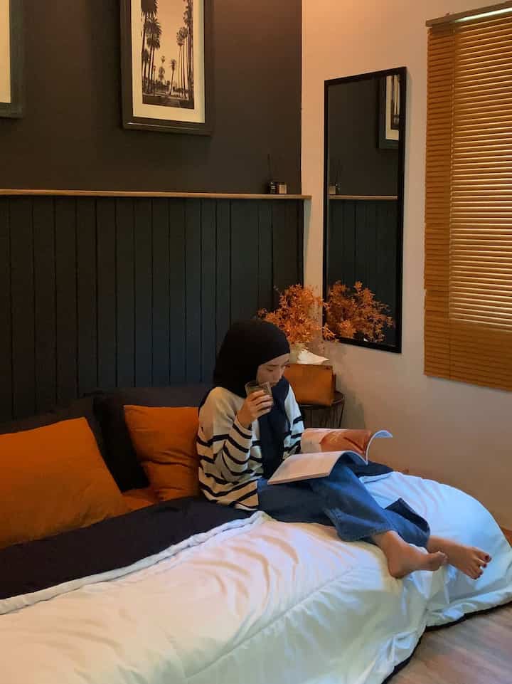 Cozy bedroom with brown and black background, featuring white bedding and orange pillows