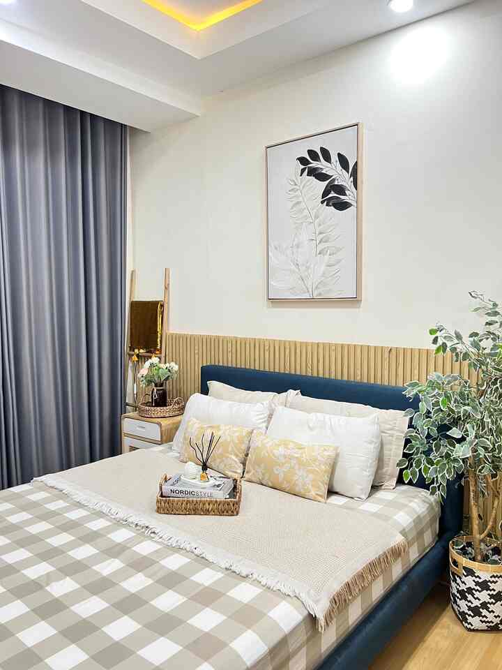 Japandi style bedroom with wood tones and white colors, featuring a centrally placed bed, nightstand, and plant creating a cozy atmosphere