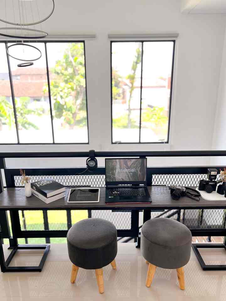 Modern black frame desk with gray stools in a two-person home office, bright windows in the background
