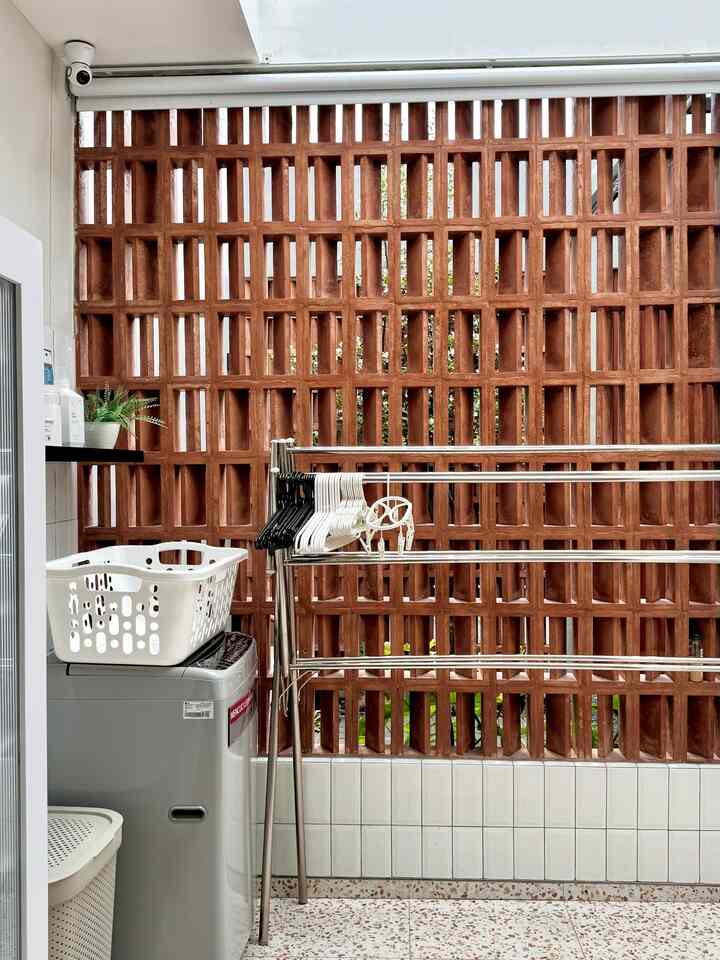 Brown brick wall and white tiled floor in a narrow balcony laundry space, featuring washing machine, drying rack, and clothes hangers