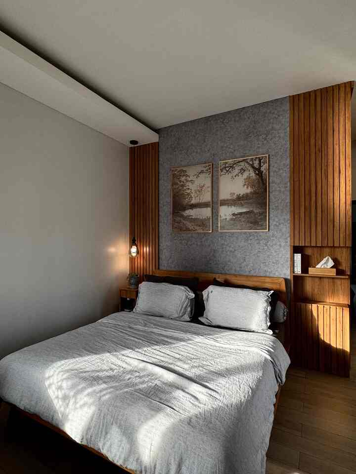 A simple bedroom with natural wood tones and white walls, featuring a large bed and framed wall art in a neat setting