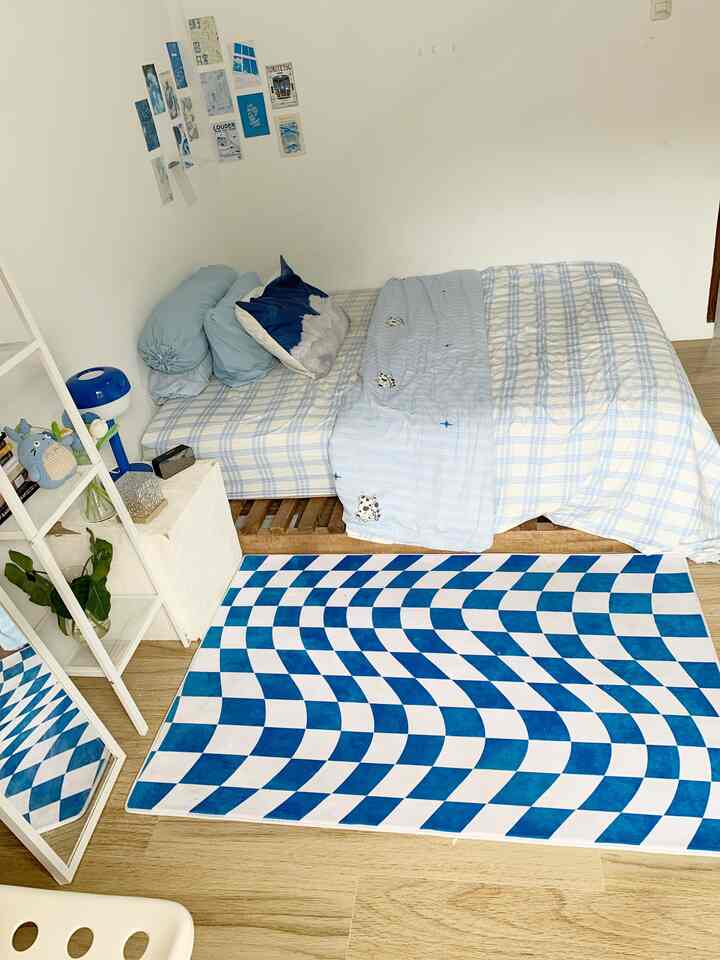 A white and blue toned small single household bedroom featuring natural wood flooring and a vibrant patterned rug in a minimal natural setting