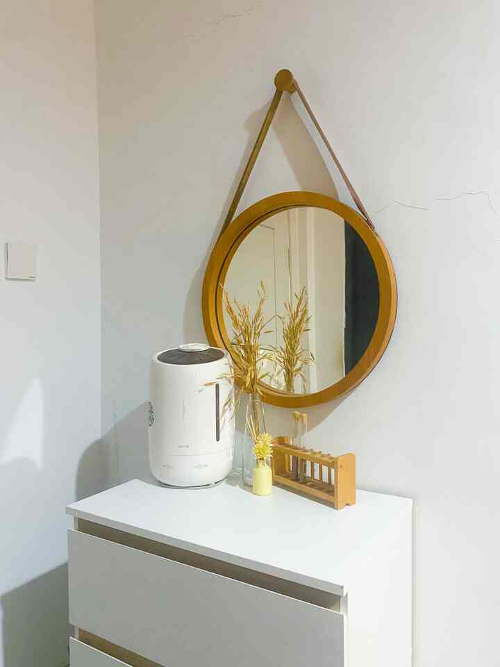 Clean space with white and wood tones featuring a round mirror and decorative items atop a small storage chest